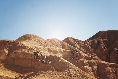 two man riding bicycle passing through brown land formations during daytime thumbnail