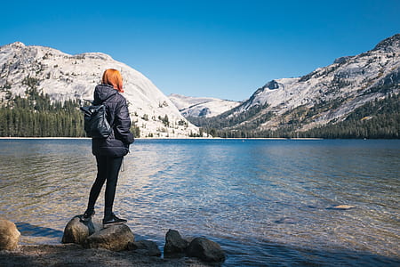 woman standing on rock facing snow-capped mountain and body of water during daytime thumbnail