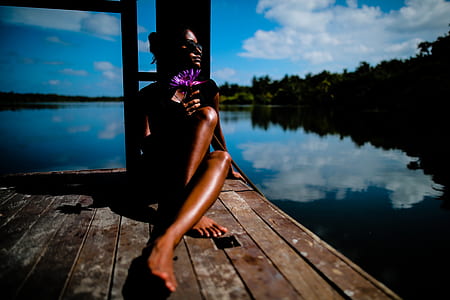 woman wearing bikini sitting on brown wooden dock near body of water thumbnail