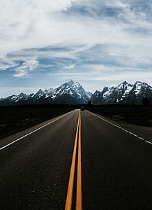 black vehicle crossing road near glacier mountains under blue sky and white clouds at daytime thumbnail