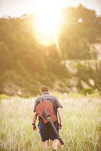 man with cut-away guitar on back walking away photo thumbnail