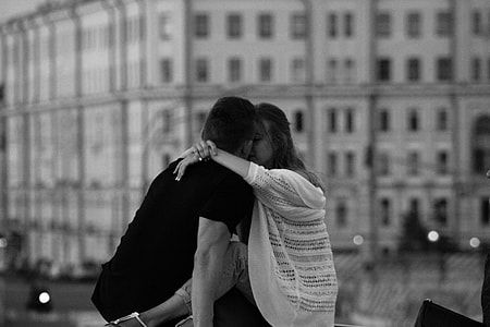 grayscale photography of woman kissing man near white building thumbnail