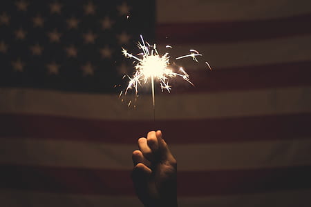 person holding lighted sparkler in front of U.S.A. flag thumbnail