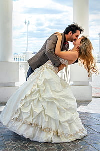 man and woman kissing near white concrete pillar during daytime thumbnail
