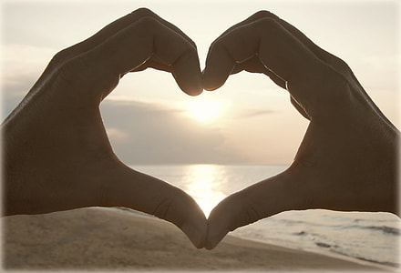 person forming heart by hands near seashore during sunset thumbnail