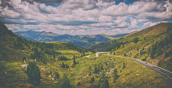Road Surrounded by Green Pine Trees Across Hills Under Blue Cloudy Sky thumbnail