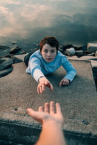 person reaching other persons hand on rock during daytime thumbnail