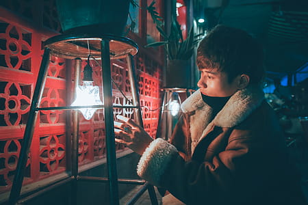 Man Wearing Brown and Gray Coat Reaching White and Black Light Bulb thumbnail