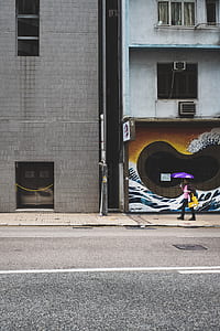 person holding purple umbrella on front of white concrete building thumbnail