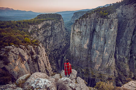 person wearing red and black plaid top standing on cliff thumbnail