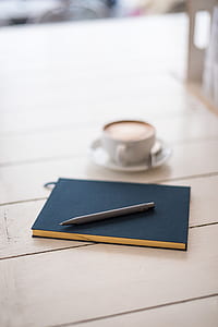 gray pen on top of blue journal book beside coffee latte thumbnail
