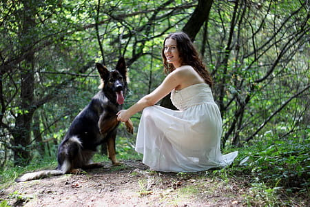 woman sitting in front of black dog surrounded by green leaf trees during daytime thumbnail