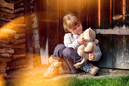 girl in grey sweater and black pants playing with brown teddy bear thumbnail