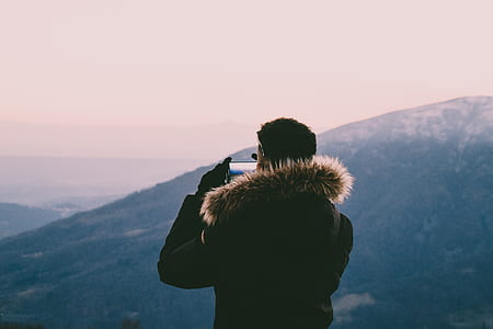 man wearing parka hoodie taking photo of mountain range thumbnail