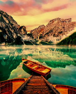 brown boat on calm body of water near mountain thumbnail