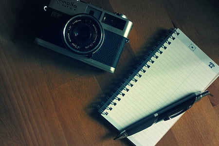 flat lay photography of grey and black Minolta MILC camera beside black lined notebook and retractable pen on wooden table thumbnail