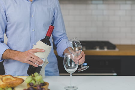 man holding wine bottle and round clear glass footed wine cup inside kitchen room thumbnail