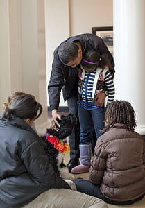 man holding black and white dog and girl in front of three women inside room thumbnail