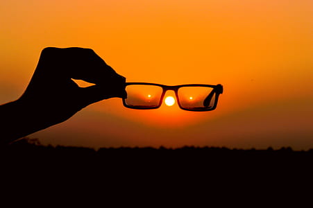 Silhouette of Person's Hand Holding Eyeglasses during Golden Hour thumbnail
