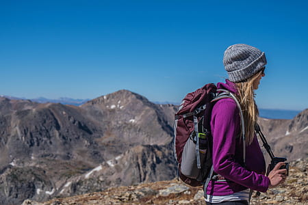 photo of smiling woman wearing purple hoodie jacket and grey knit cap standing on brown hill under clear blue sky thumbnail