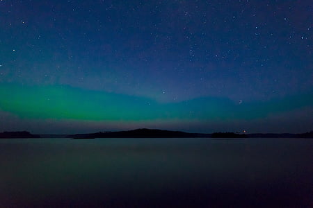 silhouette of land formation on body of water under green sky phenomenon thumbnail