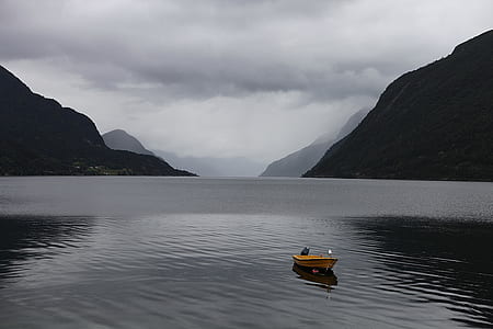 boat in the middle of lake surrounded with mountains thumbnail