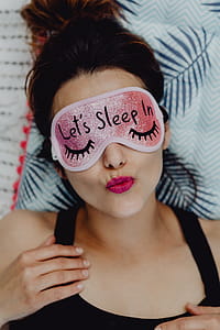 Joyful girl relaxing in bedroom - top view of brunette women in pink sleeping mask thumbnail