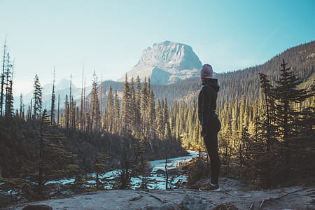 woman standing between mountain surrounded by trees thumbnail