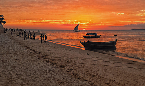 boat on brown shore sand under orange sky during daytime thumbnail