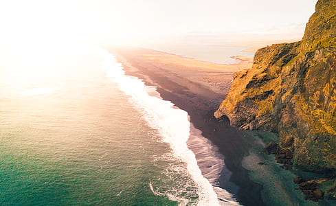 aerial photography of beach beside mountain during daytime thumbnail