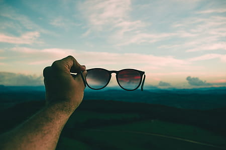 Person Holding Black Framed Sunglasses Under Blue Sky and White Clouds thumbnail