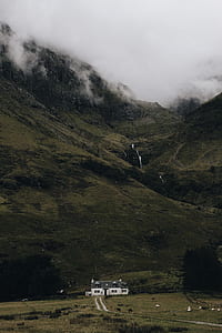 white and black house on green grass field near mountain under white clouds thumbnail