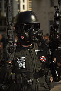 selective focus photography of man in tactical vest and mask while holding rifles thumbnail