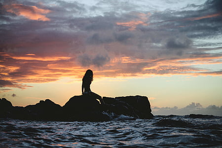 woman sitting on rock under gray sky thumbnail