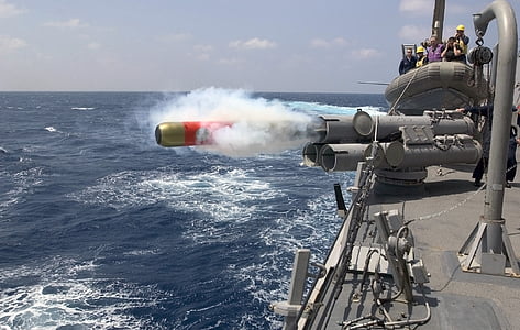 gray torpedo gun launches torpedo towards sea with watching men at distance at day thumbnail