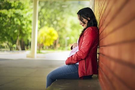 woman wearing red zip-up jacket sitting near brown wall thumbnail