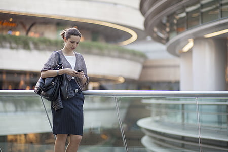 woman in grey 3/4 sleeved blazer and black skirt holding smartphone and black leather tote bag standing thumbnail