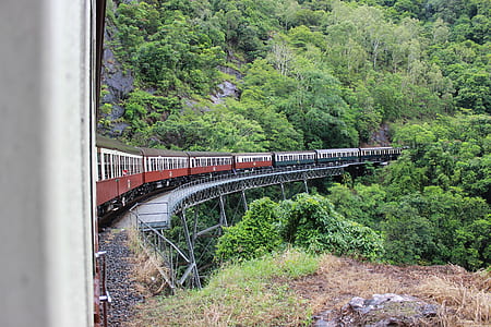 beige and red train passing bridge near mountain during daytime thumbnail