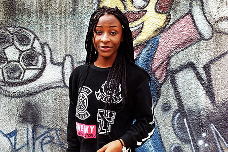 woman wearing black sweatshirt standing against mural wall thumbnail