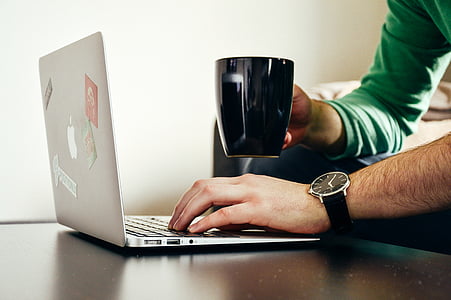 person using MacBook while holding coffee mug thumbnail