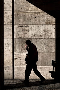 silhouette photography of man walking beside wall thumbnail