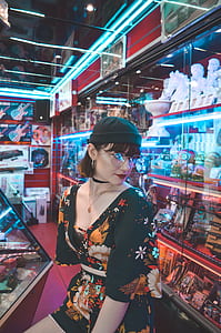 woman in black, orange, and red floral dress standing in front of glass display cabinet thumbnail