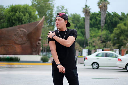 Man in Black Cap and Shirt Standing Near Cars thumbnail