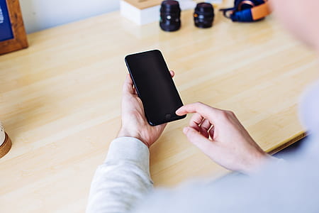person holding black iPhone 7 leaning on brown wooden desk thumbnail