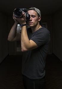 man holding black Canon DSLR camera standing in dim room thumbnail