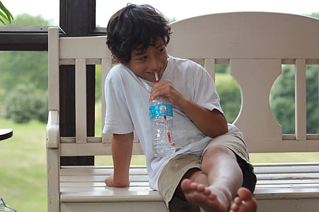 boy sitting on white bench sipping plastic labeled bottle thumbnail