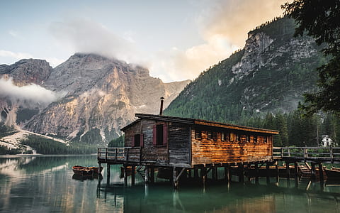 brown wooden bungalow on body of water with rowboat near mountain thumbnail