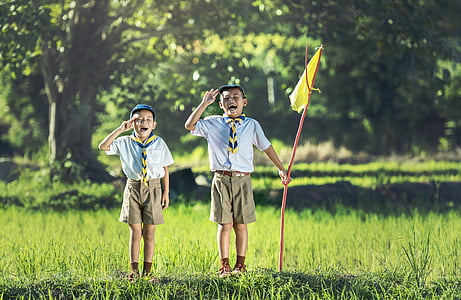 boy's scouts standing on green grass while holding flag thumbnail