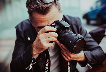 man in black jacket holding black Canon DSLR camera thumbnail