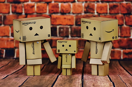 three brown Amazon cardboard human-designed boxes standing on brown surface near brick wall thumbnail